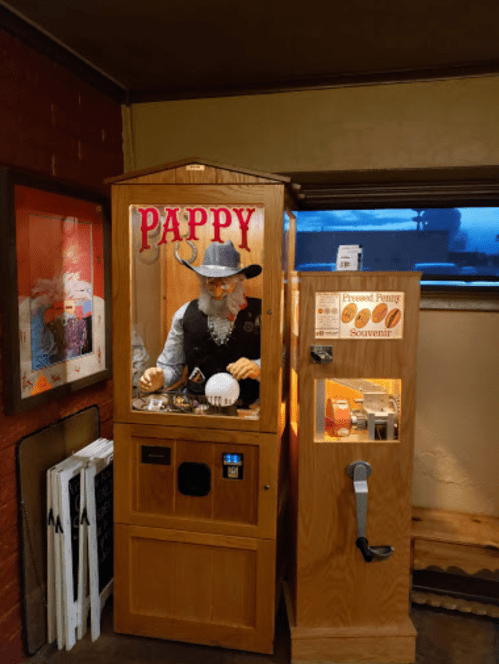 A vintage wooden vending machine with a figure labeled "PAPPY" and a sign for a pressed penny souvenir.